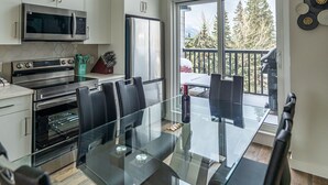 A modern kitchen with white cabinets, stainless steel appliances, and a glass dining table with black chairs. - Skyline-Townhouse Combo-AC-Pool-Hot Tub (Canmore)