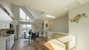 A modern kitchen with white cabinets, a dining area with a table and chairs, a patterned sofa, and a wooden bench. - Skyline-Townhouse Combo-AC-Pool-Hot Tub (Canmore)