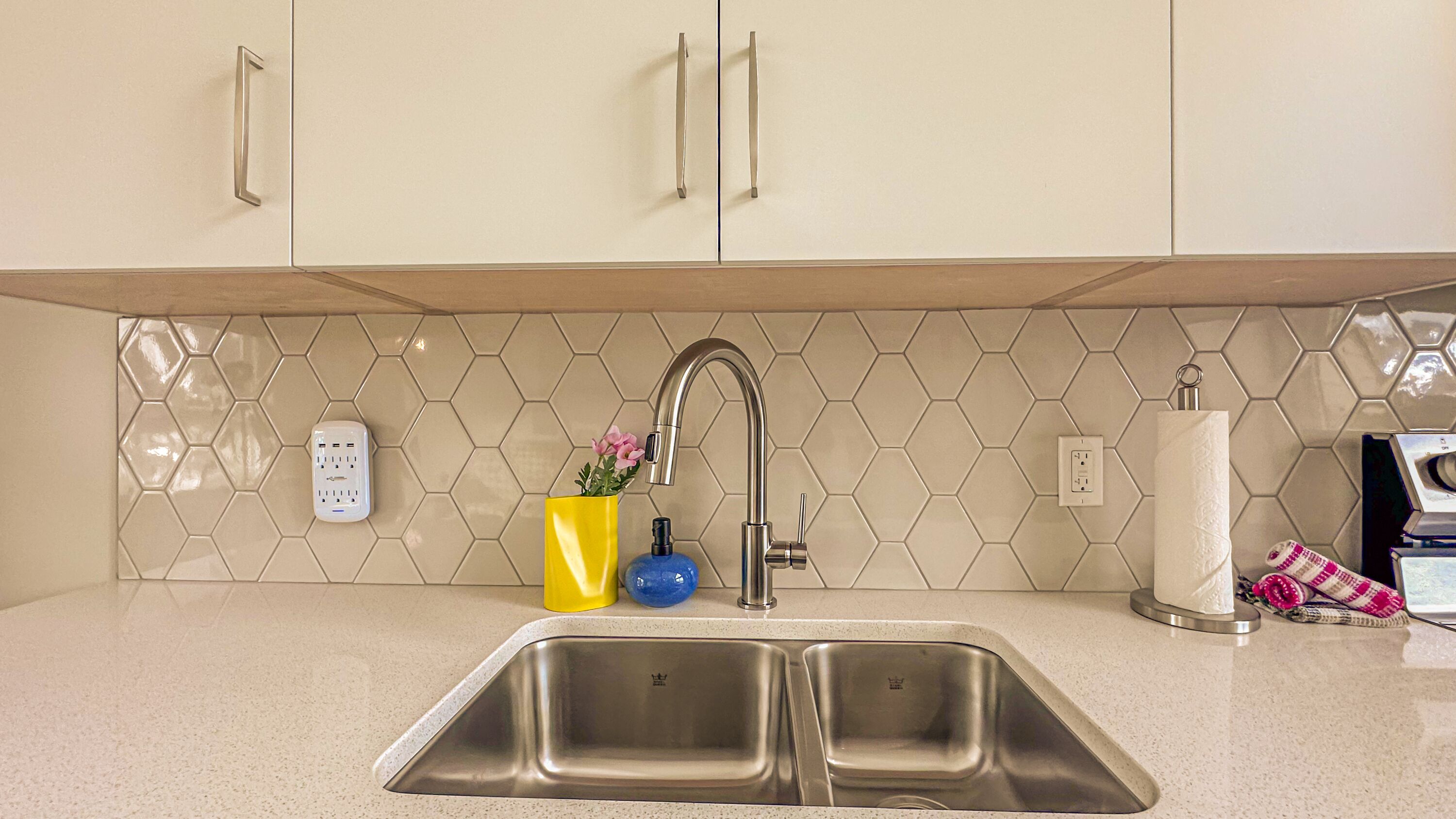 A kitchen with two stainless steel sinks, a yellow vase with flowers, a blue soap dispenser, and a white paper towel holder.