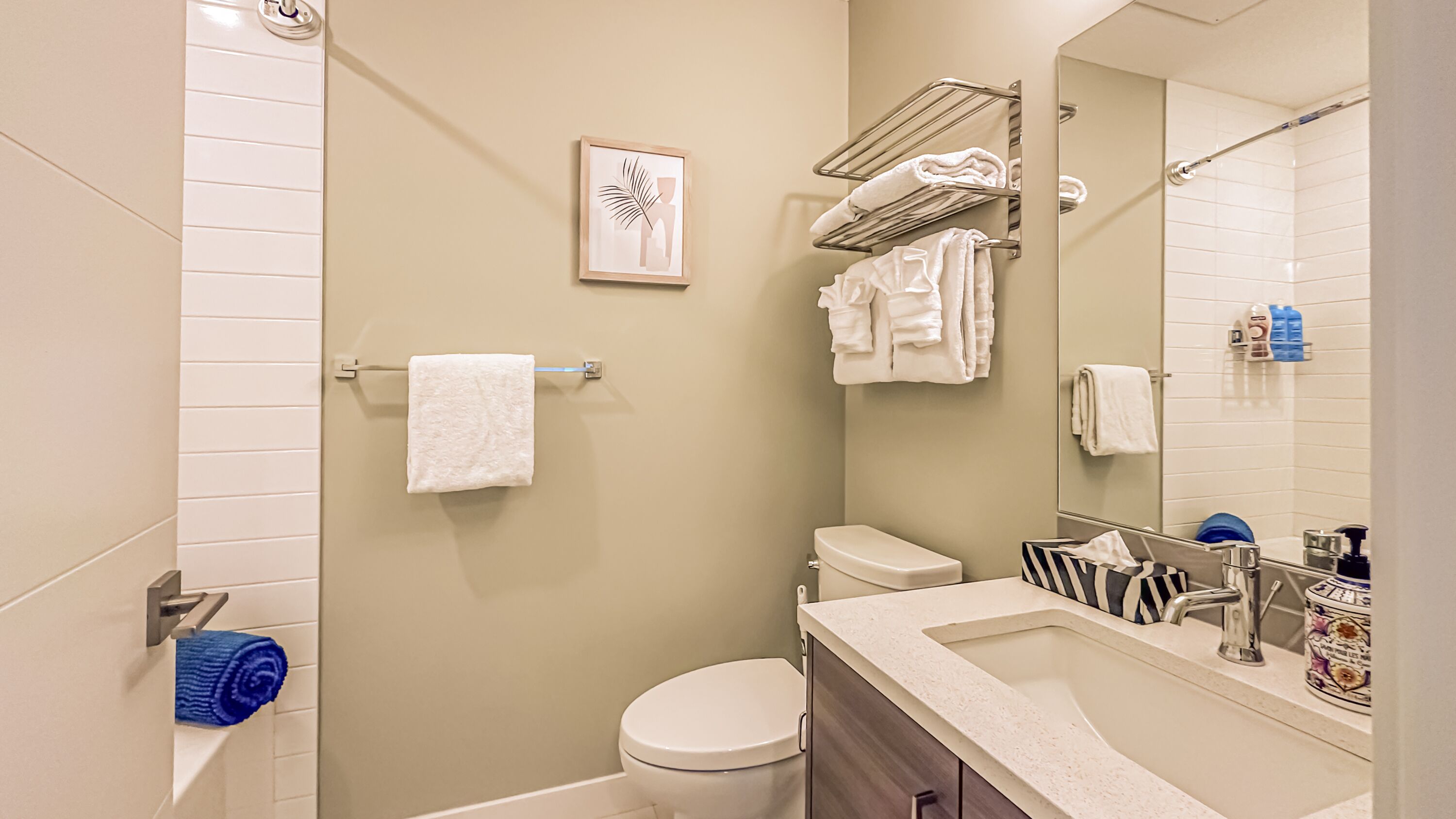 A modern bathroom with a toilet, sink, and shower. There are towels on a rack and a framed picture on the wall.
