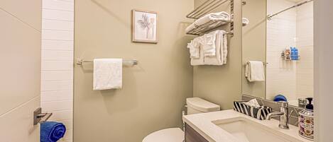 A modern bathroom with a toilet, sink, and shower. There are towels on a rack and a framed picture on the wall.