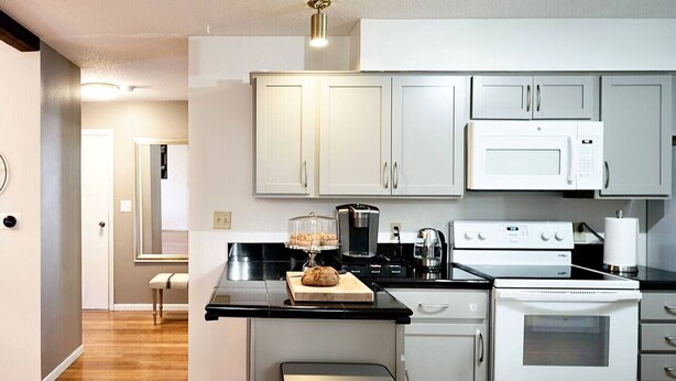 A modern kitchen with white cabinets, a black countertop, stainless steel appliances, and a wooden floor. - Blue House Cozy Getaway (Sioux Falls)