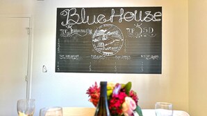 A dining table set with wine glasses, a vase with flowers, and a chalkboard menu titled 'Blue Hulse' with sections for breakfast, lunch, dinner, and bars. - Blue House Cozy Getaway (Sioux Falls)