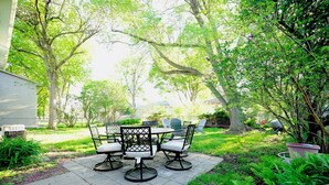 An outdoor patio with a table and chairs, surrounded by lush greenery and trees. - Blue House Cozy Getaway (Sioux Falls)