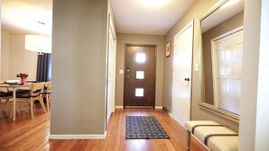 A hallway with wooden flooring, a dining area with a table and chairs, and a bench. - Blue House Cozy Getaway (Sioux Falls)