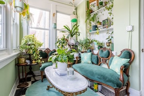 Una habitación acogedora con un sofá verde, una mesa de centro de mármol y varias plantas en macetas.