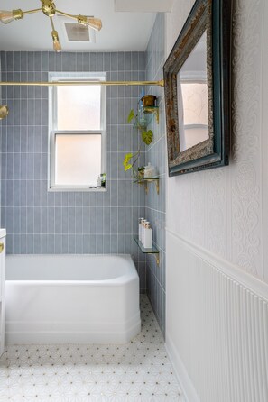 Et badeværelse med badekar, et vindue og et spejl på væggen.