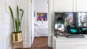 A modern living room with a flat-screen TV, a potted plant, and a colorful abstract painting on the wall. - Classic Chicago 2 Flat transformed into a Parisian plant lovers paradise (Chicago)