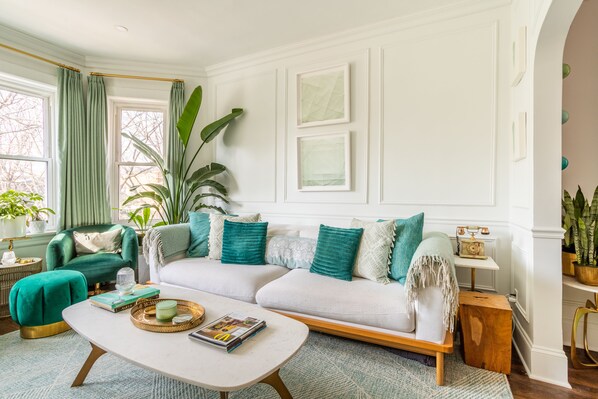 A living room with a white sofa, teal cushions, a coffee table, and a large plant.