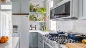 A modern kitchen with white cabinets, a built-in oven, a stove, and a microwave. There are plants on the shelves and a bowl of oranges on the counter. - Classic Chicago 2 Flat transformed into a Parisian plant lovers paradise (Chicago)