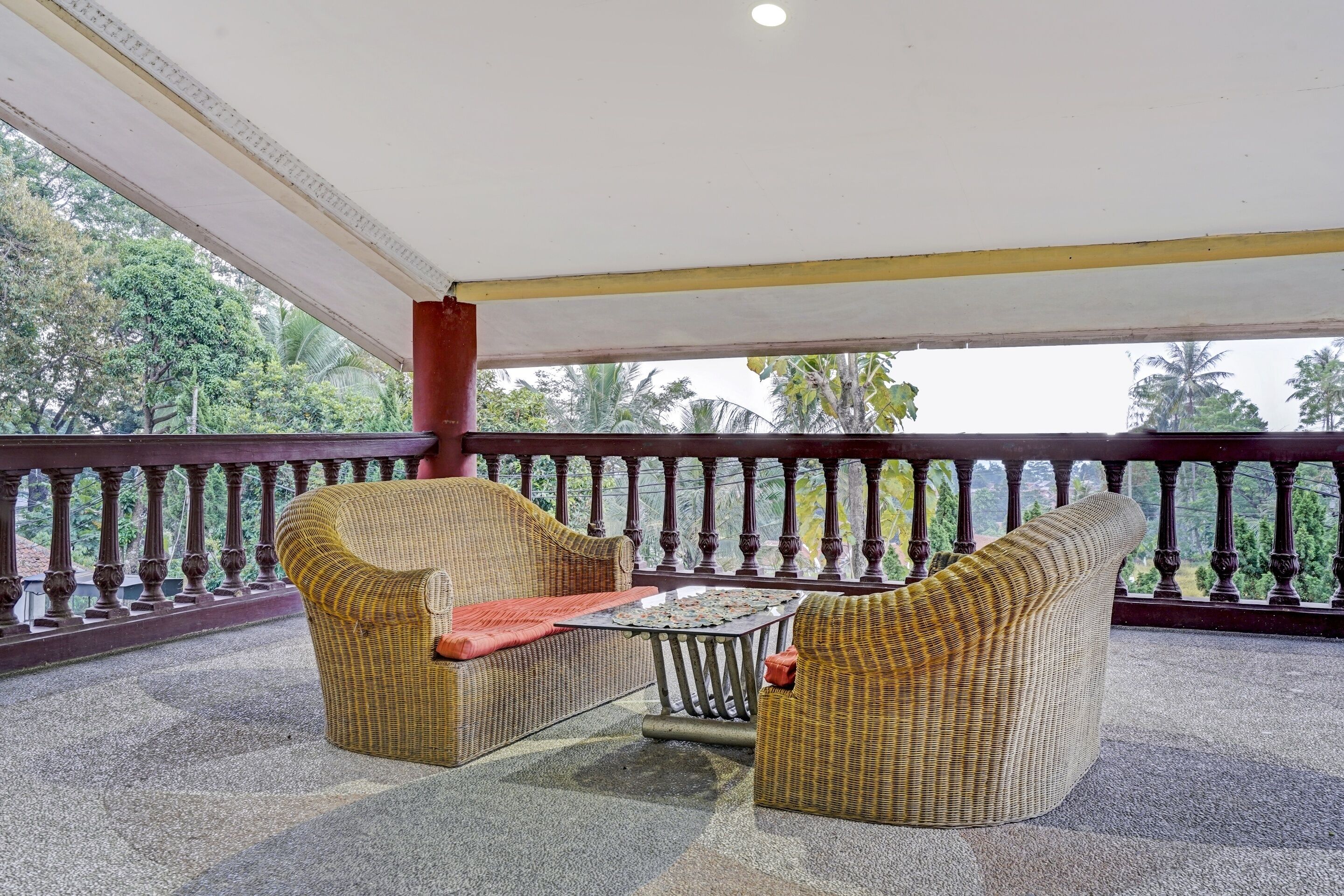 A covered balcony with wicker furniture, a small table, and a railing with decorative balusters.