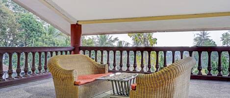 A covered balcony with wicker furniture, a small table, and a railing with decorative balusters.