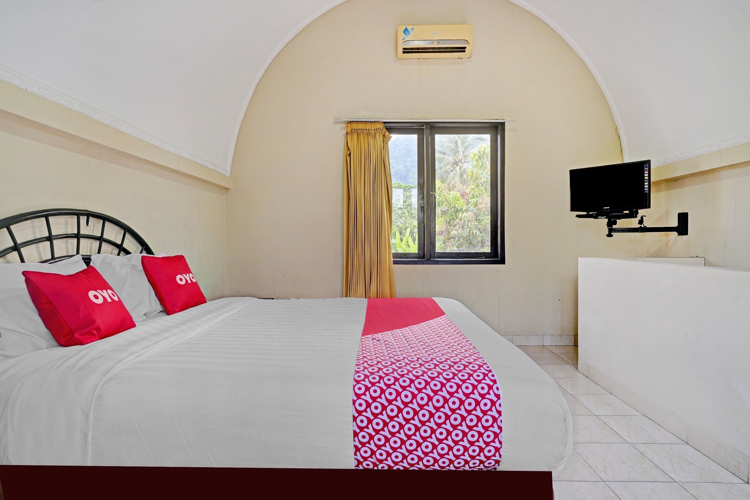 A hotel room with a bed, a TV, a window with curtains, and an air conditioning unit.