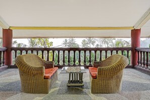 Un espacio exterior techado con mobiliario de mimbre y una mesa central.