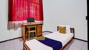 Un dormitorio con cama, escritorio con silla, computadora y ventana con cortinas rojas.