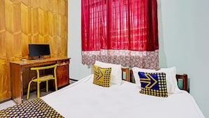 Una habitación con escritorio de madera, computadora, silla y cama con almohadones estampados.