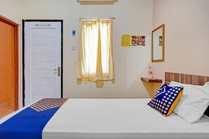 A hotel room with a bed, a window with curtains, a nightstand with a bottle, and a mirror on the wall.