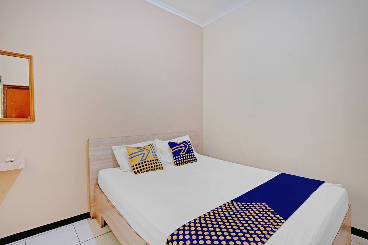 A neatly made bed with a white and blue patterned bedspread, two pillows with geometric designs, and a wooden headboard.
