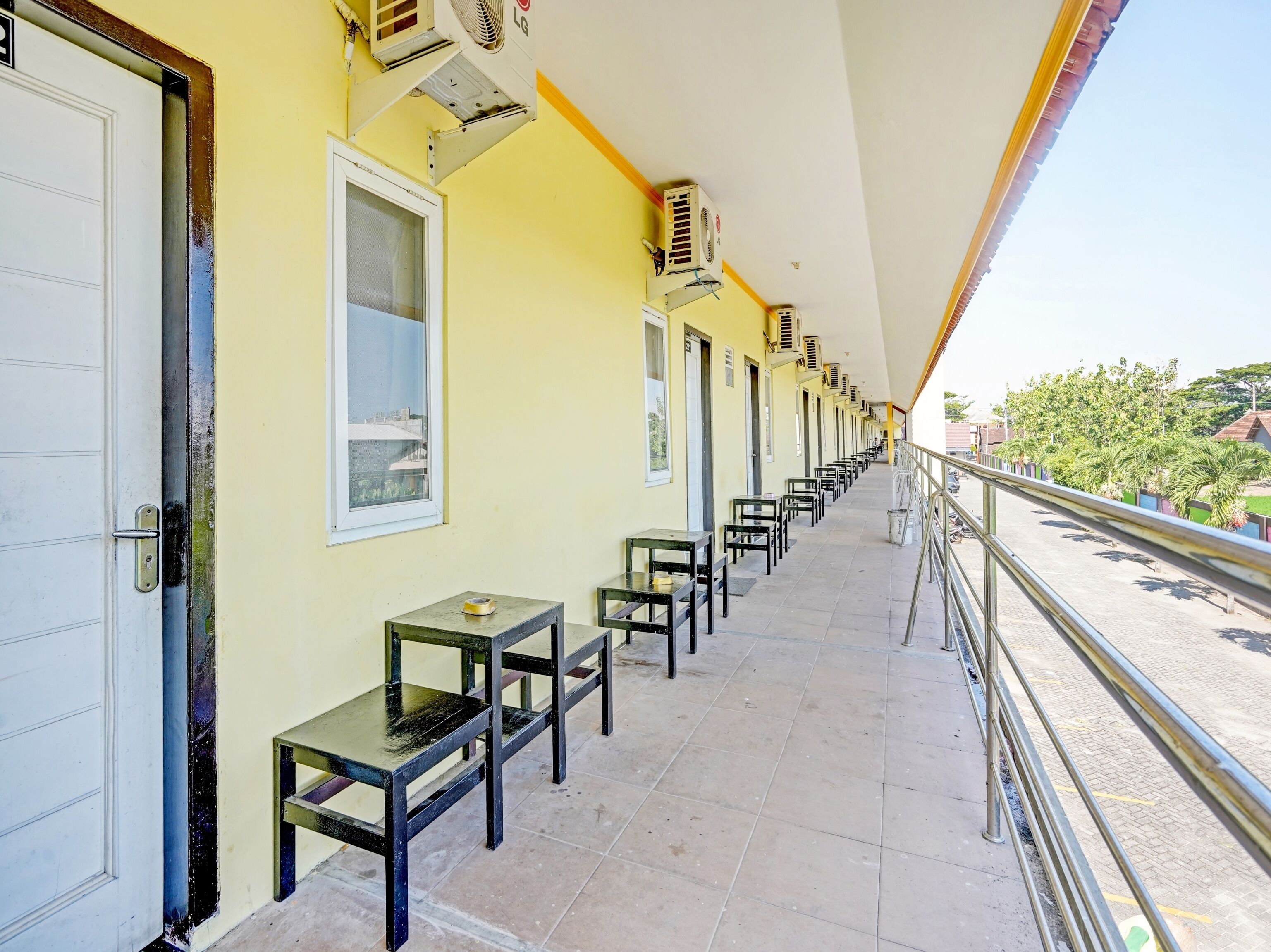 Un couloir bordé de rangées de tables et de chaises, équipé de climatiseurs, et doté d’un balcon avec une balustrade.