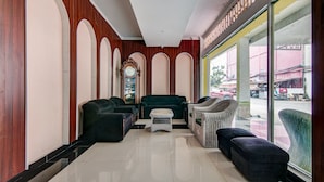 Un hall d’entrée avec un canapé vert, des fauteuils noirs et des chaises en osier.