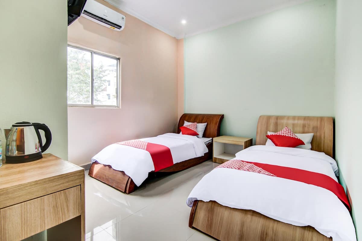 Une chambre d’hôtel avec deux lits en bois, une table de chevet en bois, une lampe de chevet, une fenêtre et un appareil de climatisation.
