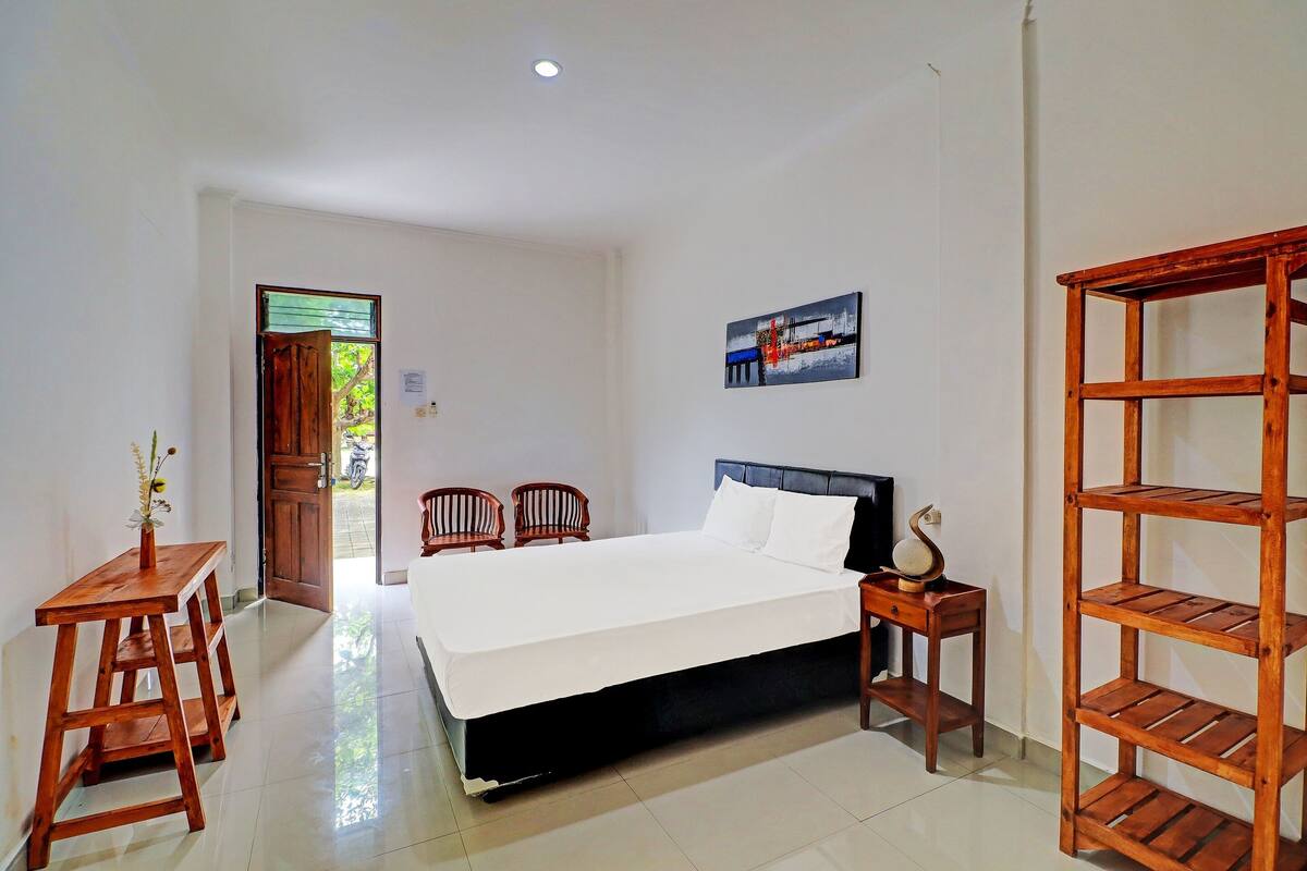 A bedroom with a bed, wooden nightstands, a wooden shelf, and a painting on the wall.