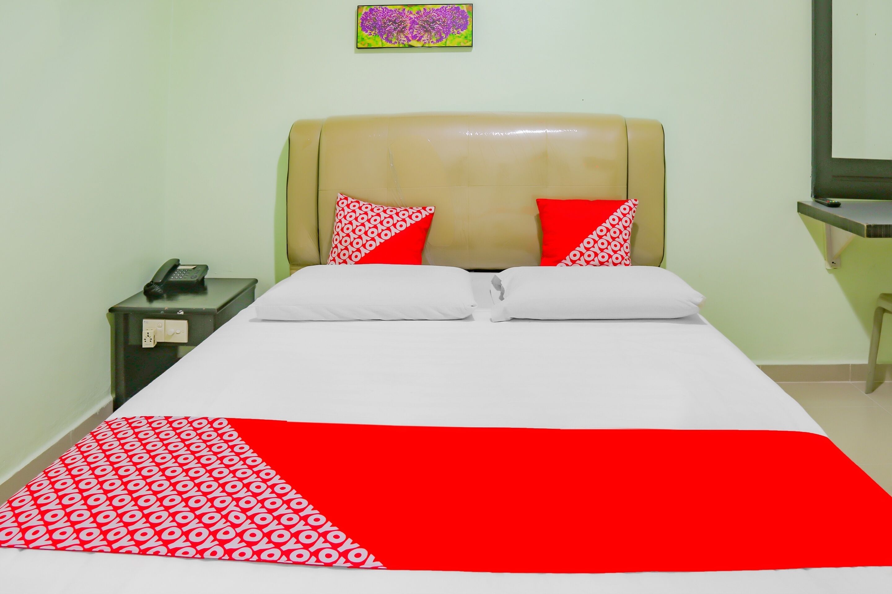 A bed with a red and white patterned bedspread, two white pillows, and a beige headboard.
