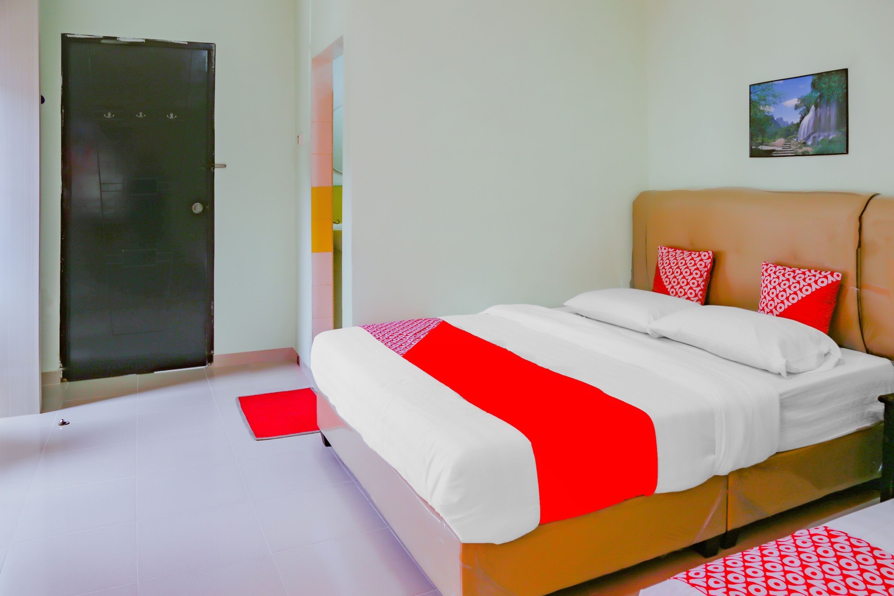 A hotel room with a bed, a door, and a painting on the wall.
