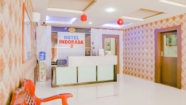 A hotel reception area with a reception desk, a water dispenser, and a seating area with a chair. - OYO 90269 Hotel Indorasa 2 (Batam)