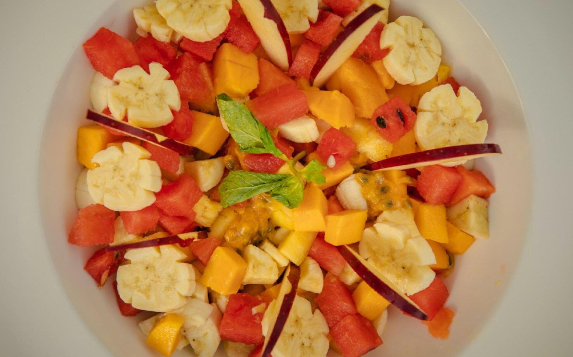 A fruit salad with various fruits and a mint leaf.