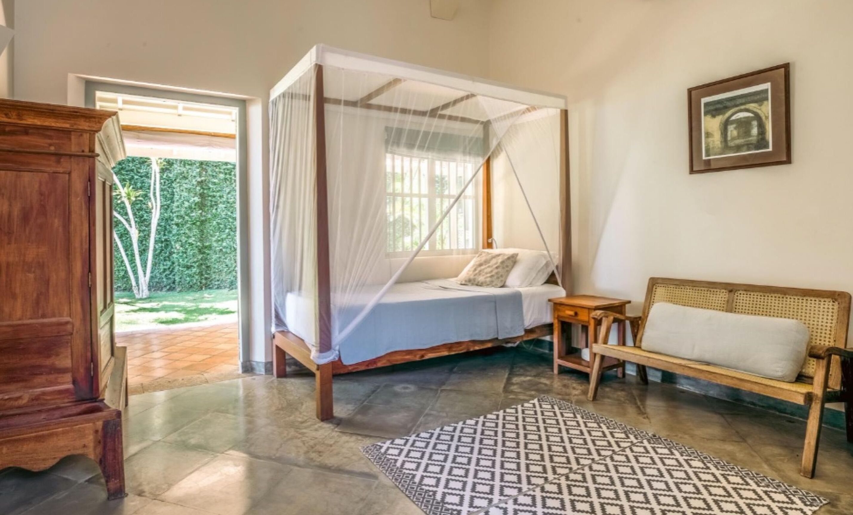 A room with a four-poster bed, a wooden bench, a patterned rug, and a framed picture on the wall.