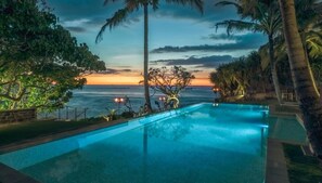 A swimming pool with a sunset view, surrounded by palm trees and a stone wall. - Elevated Family Beach Villa Overlooking Surf Break (Weligama)