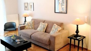 Un salon comprenant un canapé, deux tables d’appoint avec des lampes, une table basse et un lustre.