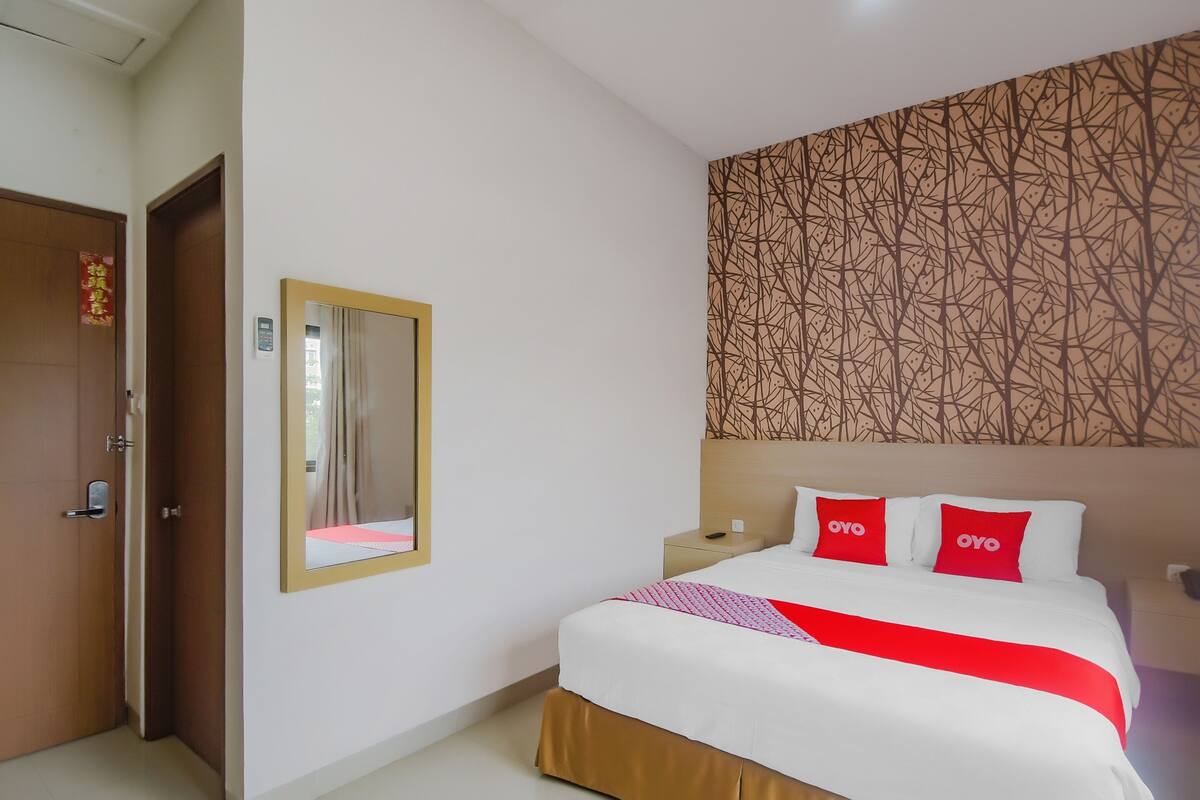 A hotel room with a bed, a nightstand, a mirror, and a door.