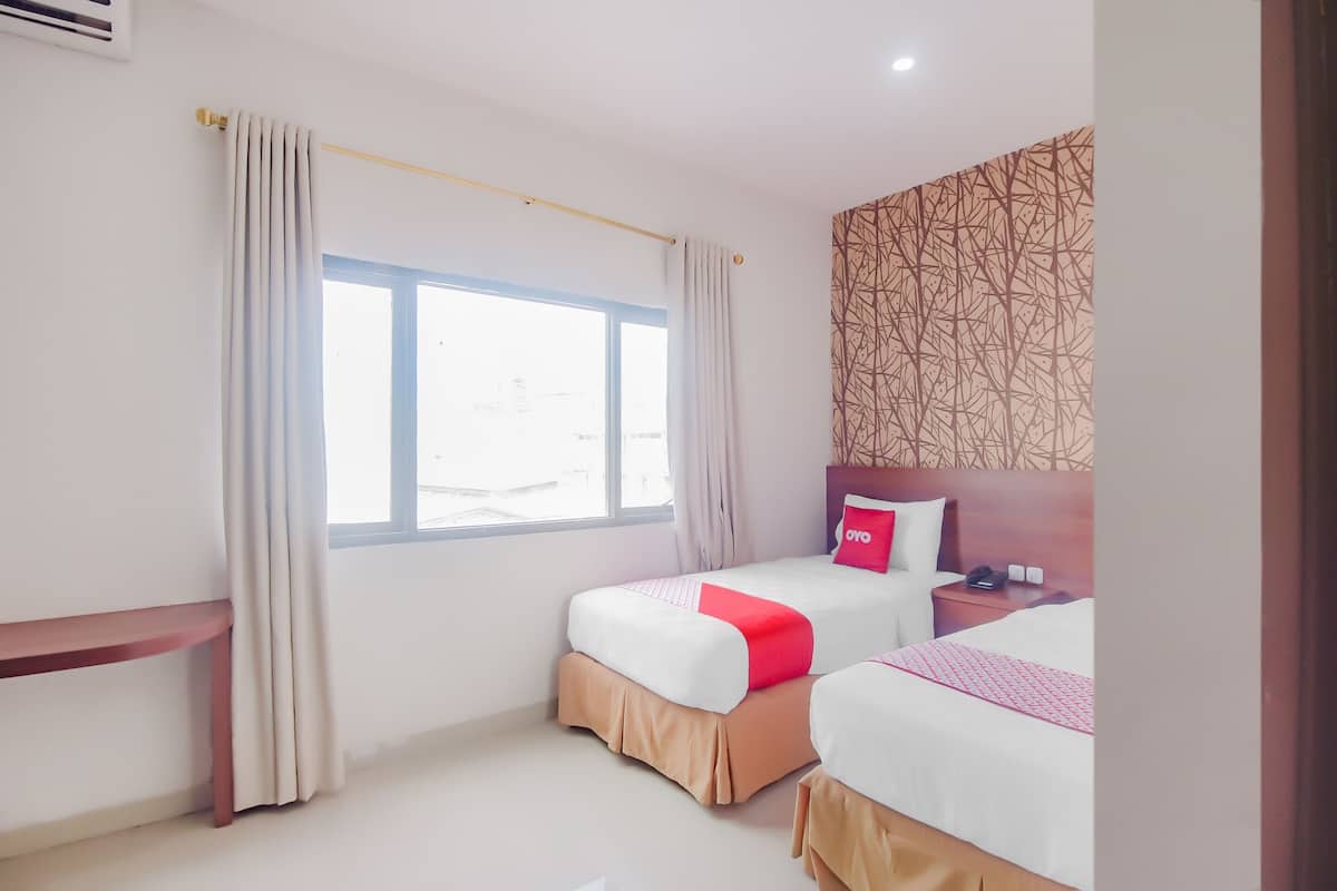 A hotel room with two beds, a bedside table, a nightstand, and a window with curtains.