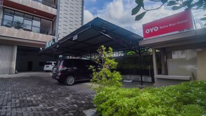 Entrada de un hotel con una zona de estacionamiento techada, un letrero que indica OYO Bahu Bay Hotel, y un edificio con varios balcones.