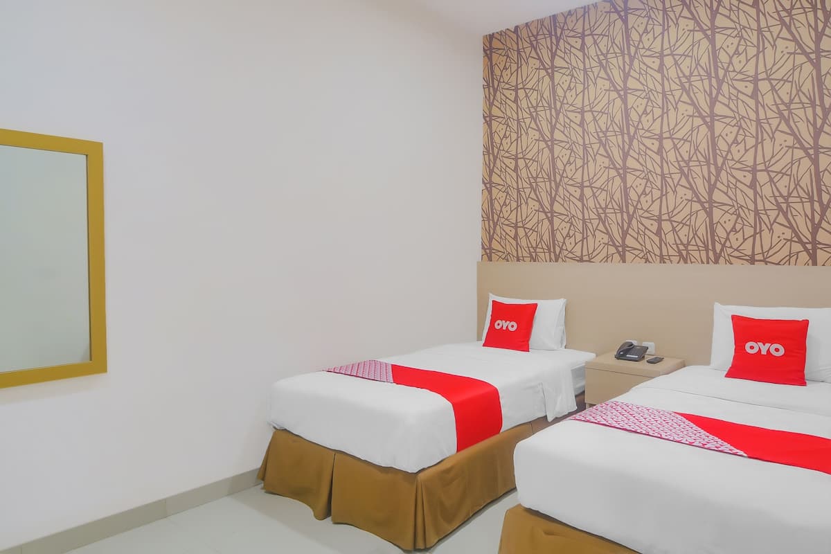 A hotel room with two beds, each with white bedding and red accents, a patterned wallpaper, and a mirror on the wall.