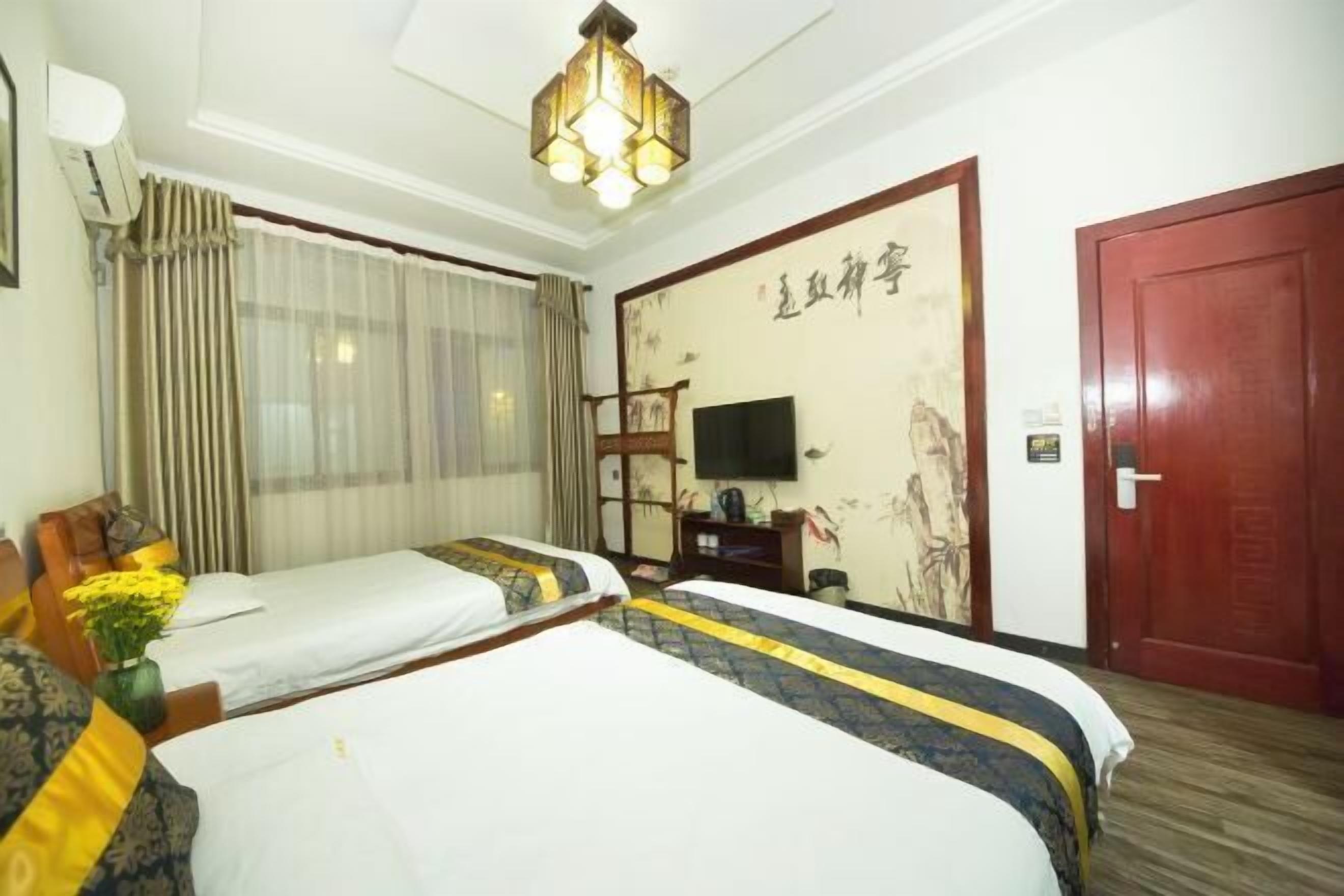 Habitación de hotel con dos camas, un televisor, una pared decorada con obras de arte y una puerta roja.