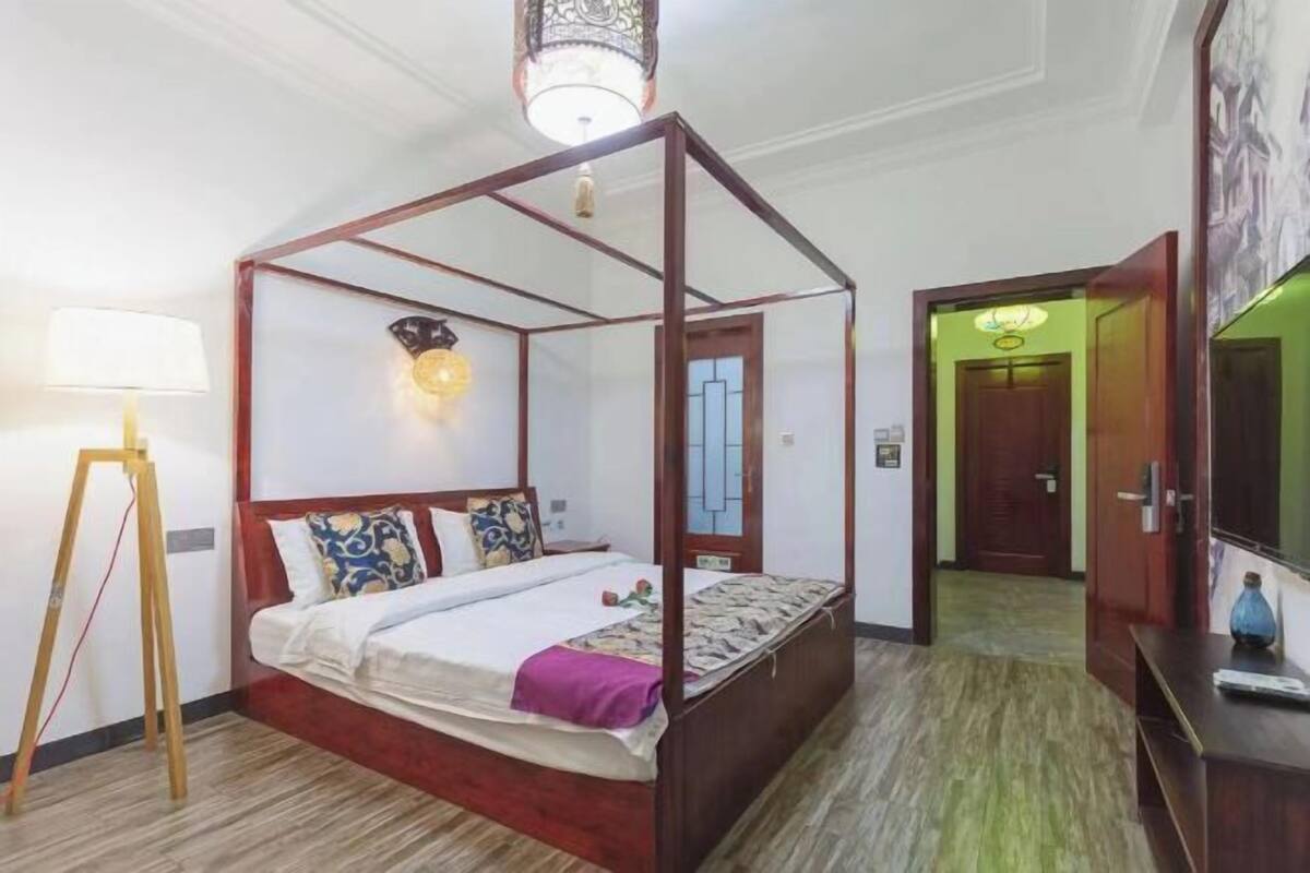 Ein Bett mit Baldachin und Holzrahmen, eine stehende Lampe und eine an der Wand befestigte Leuchte.
