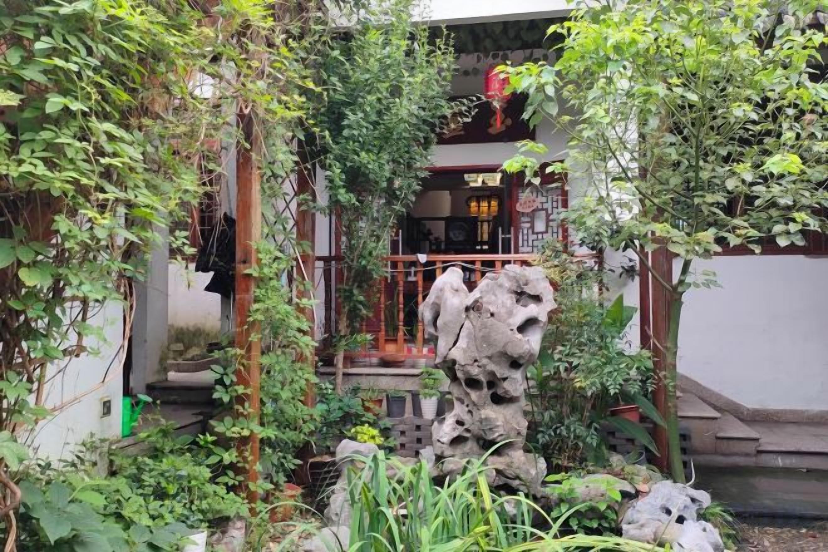 Un patio con una formación rocosa, vegetación y un edificio de diseño tradicional.