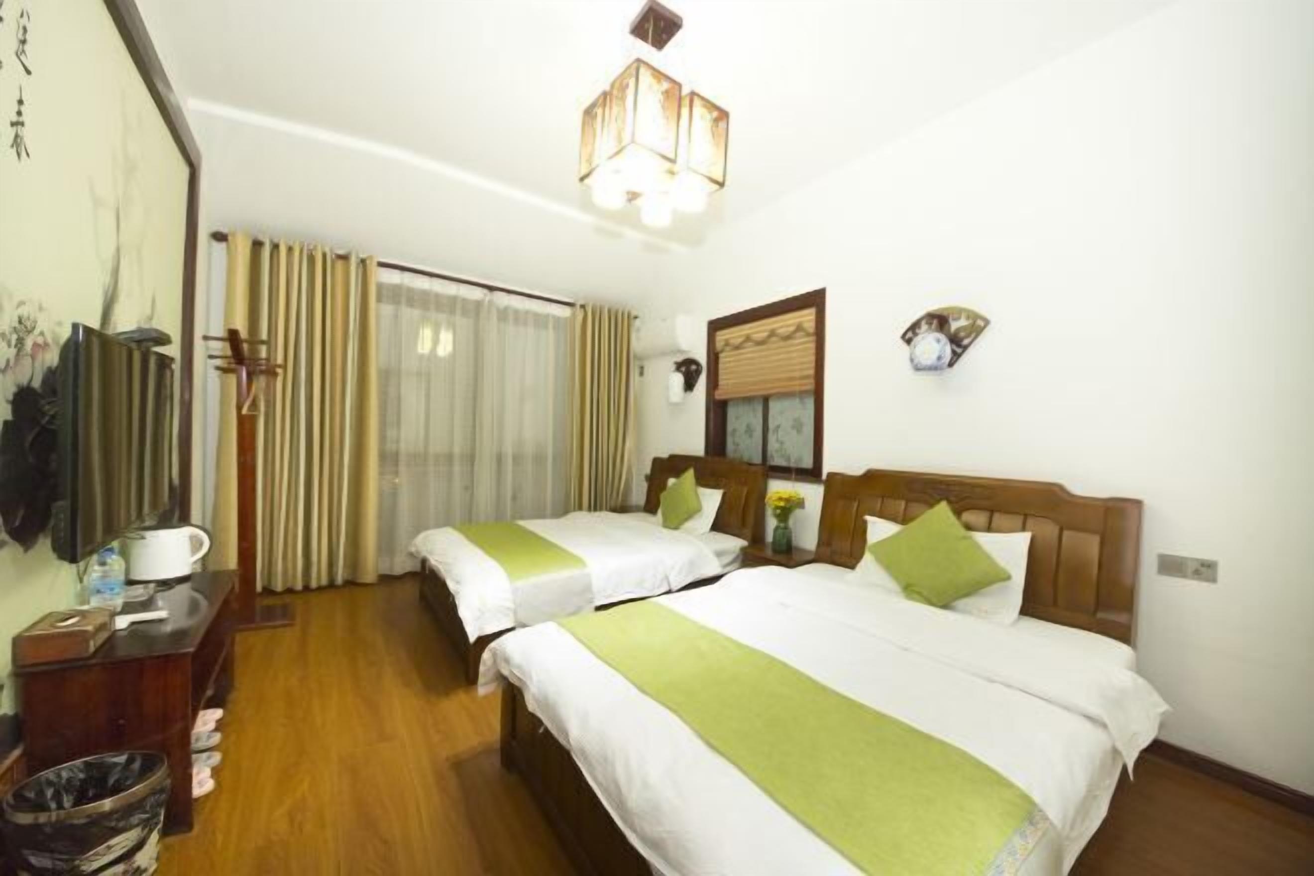 A hotel room with two beds, a wooden headboard, a nightstand, a desk, a chair, a trash bin, and a window with curtains.