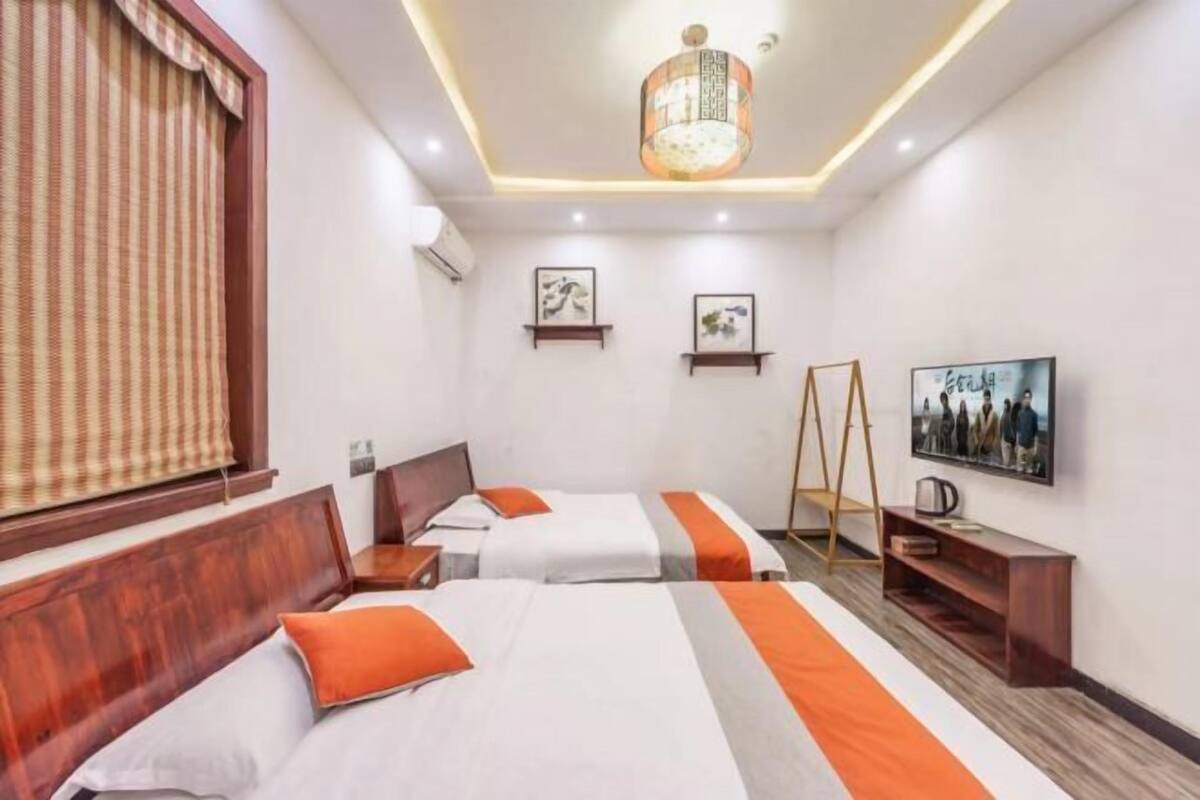 Ein Hotelzimmer mit zwei Betten, einem hölzernen Kopfteil, einer stehenden Leiter, einem Fernseher und Kunstwerken an den Wänden.