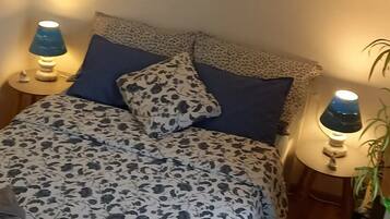 Een bed met een deken met bloemendesign, twee kussens, een bedlampje en een nachtkastje met een plantje.