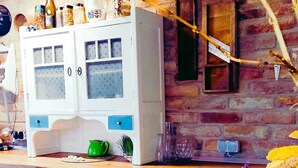 Una cocina rústica con pared de ladrillo, techo de madera y un armario blanco con puertas de cristal.