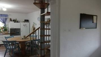 Une cuisine avec un coin repas, un escalier en bois et un téléviseur fixé au mur.