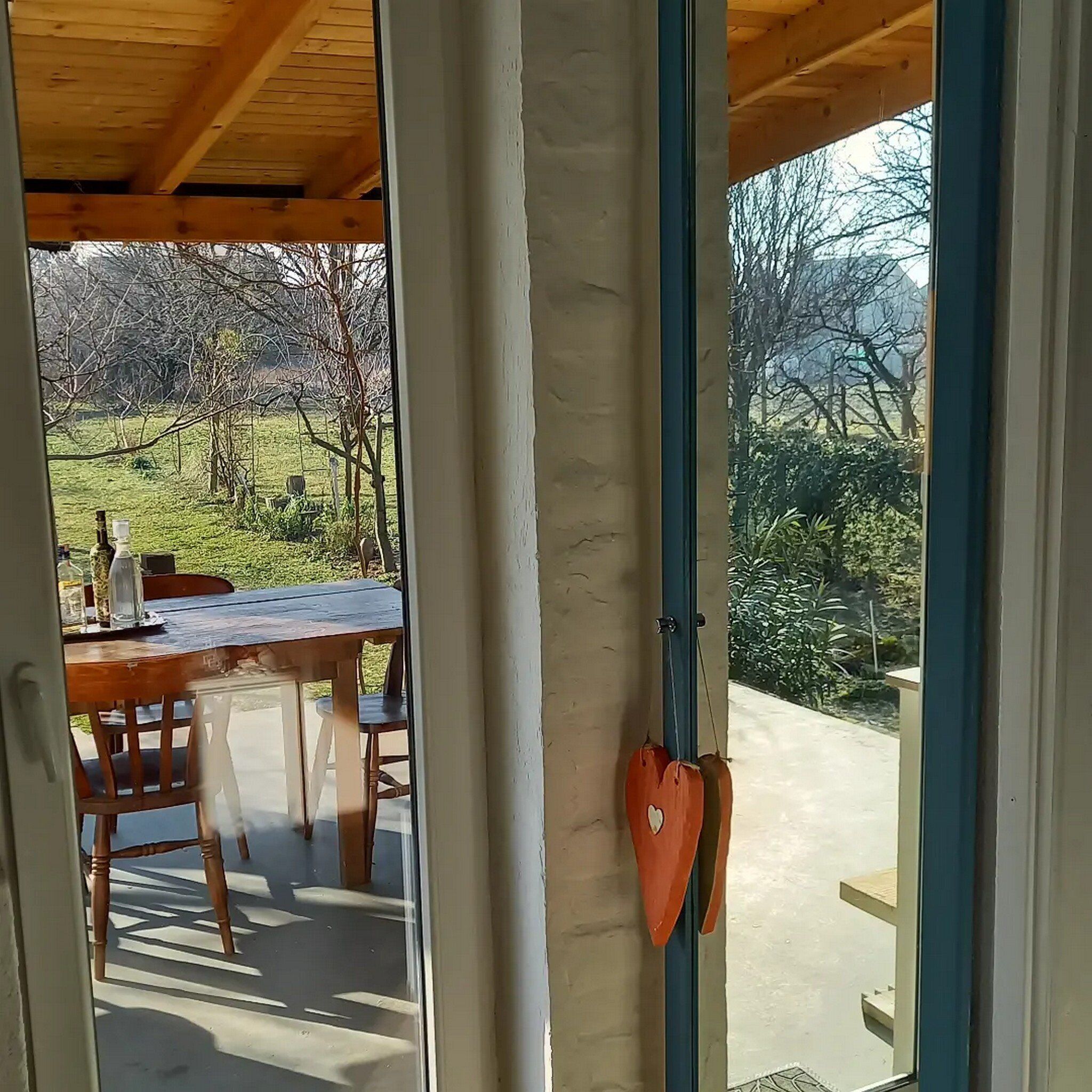 Un'area esterna coperta con tavolo e sedie, una decorazione a forma di cuore e vista su un giardino e alberi.