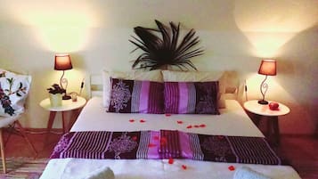 A hotel room with a neatly made bed, two bedside lamps, a decorative plant, and a small table with a fruit.