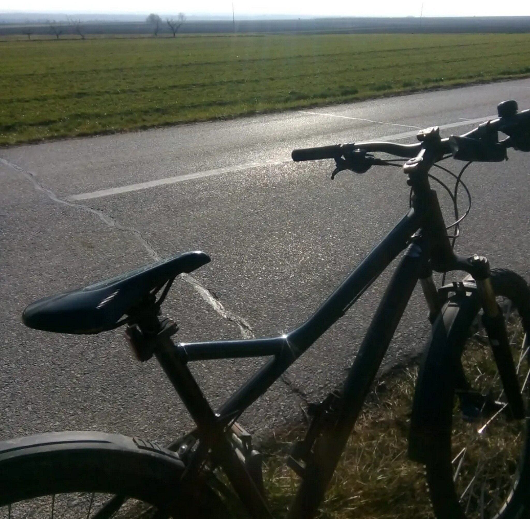 A bicycle parked on a rural road with a grassy field in the background.