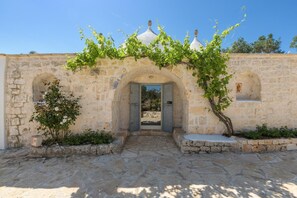 A stone building with an arched entrance, a small shrine, and a vine-covered wall. - Trullo Cecapesce con Piscina by Wonderful Italy (Carovigno)