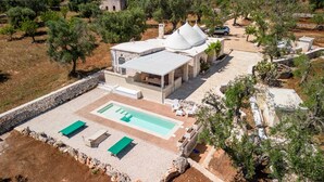 A modern villa with a swimming pool, outdoor seating, and a stone wall surrounding the property.